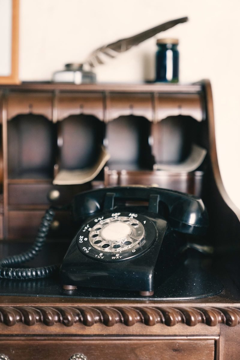 Black rotary telephone on a dark wooden writing desk with paper pigeonholes
