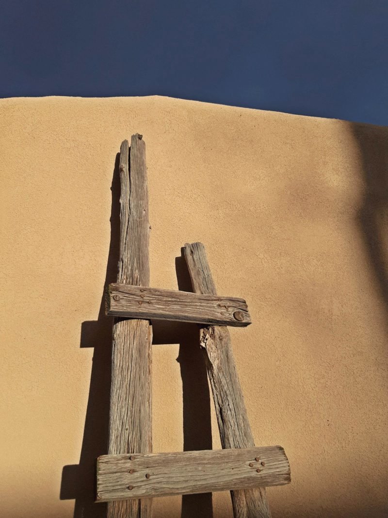Weathered wooden ladder leaning on an adobe wall under a dark blue sky