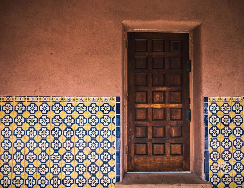 Heavy wooden door set in an adobe wall with blue and yellow tile wainscot
